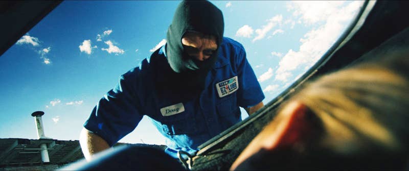 A masked man, labeled &quot;Daniel&quot; on a service uniform, appears to be interacting with someone inside a car trunk on a sunny day