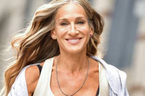 Sarah Jessica Parker smiles, wearing a sleeveless top and a necklace, with her long hair flowing