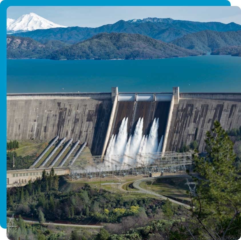A dam releasing water with mountains and a lake in the background