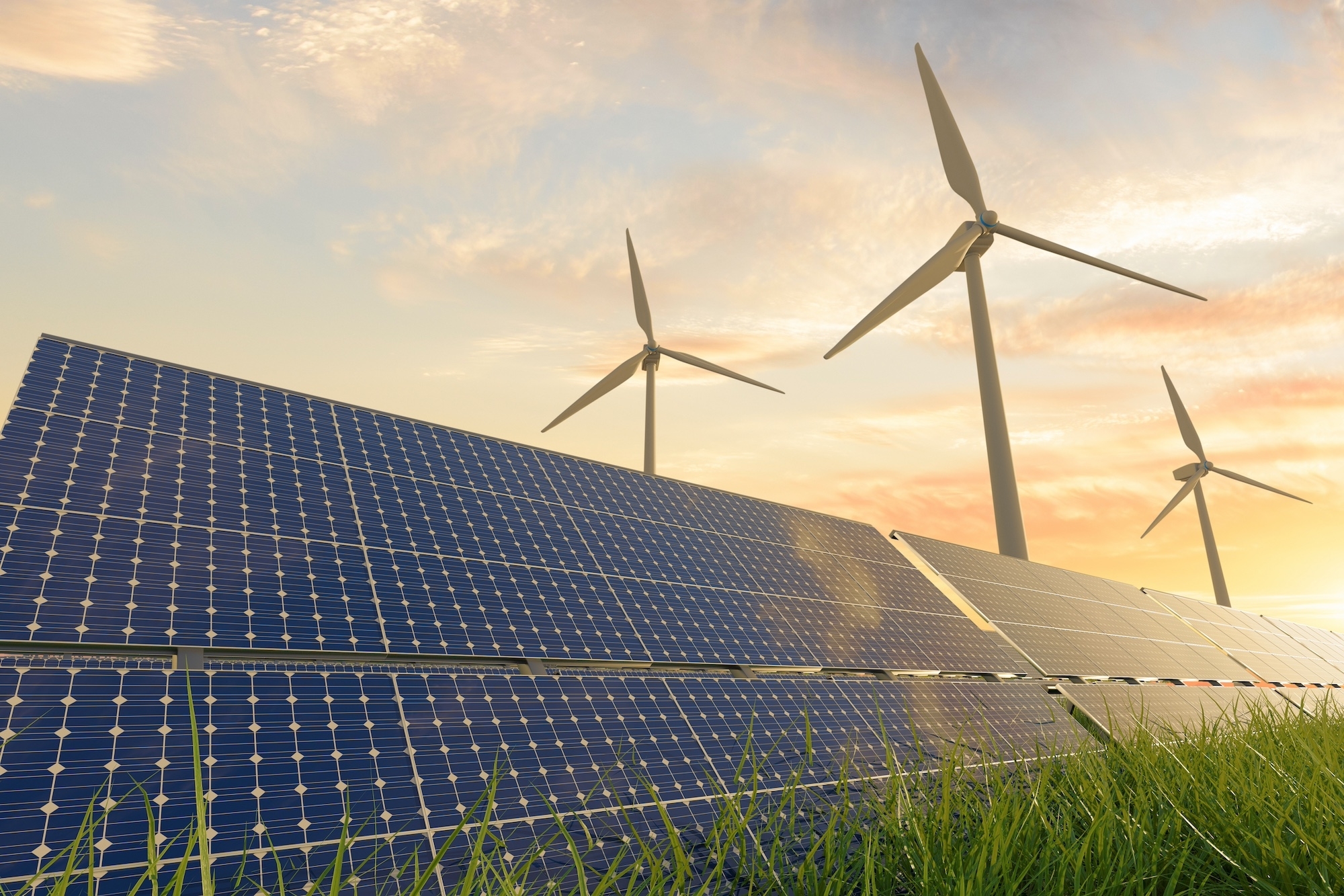 Wind turbines and solar panels in a field of grass with a sunset sky in the background, illustrating renewable energy sources