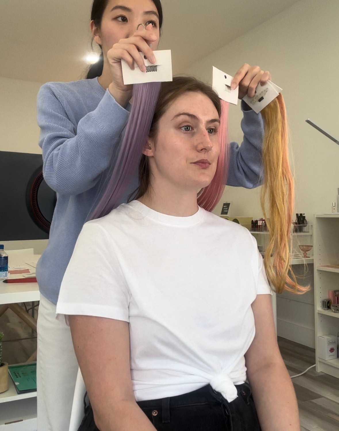 Kim Kardashian seated, having hair extensions applied by a stylist