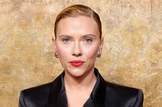 Scarlett Johansson wearing a sleek black jacket with her hair slicked back in front of a textured backdrop