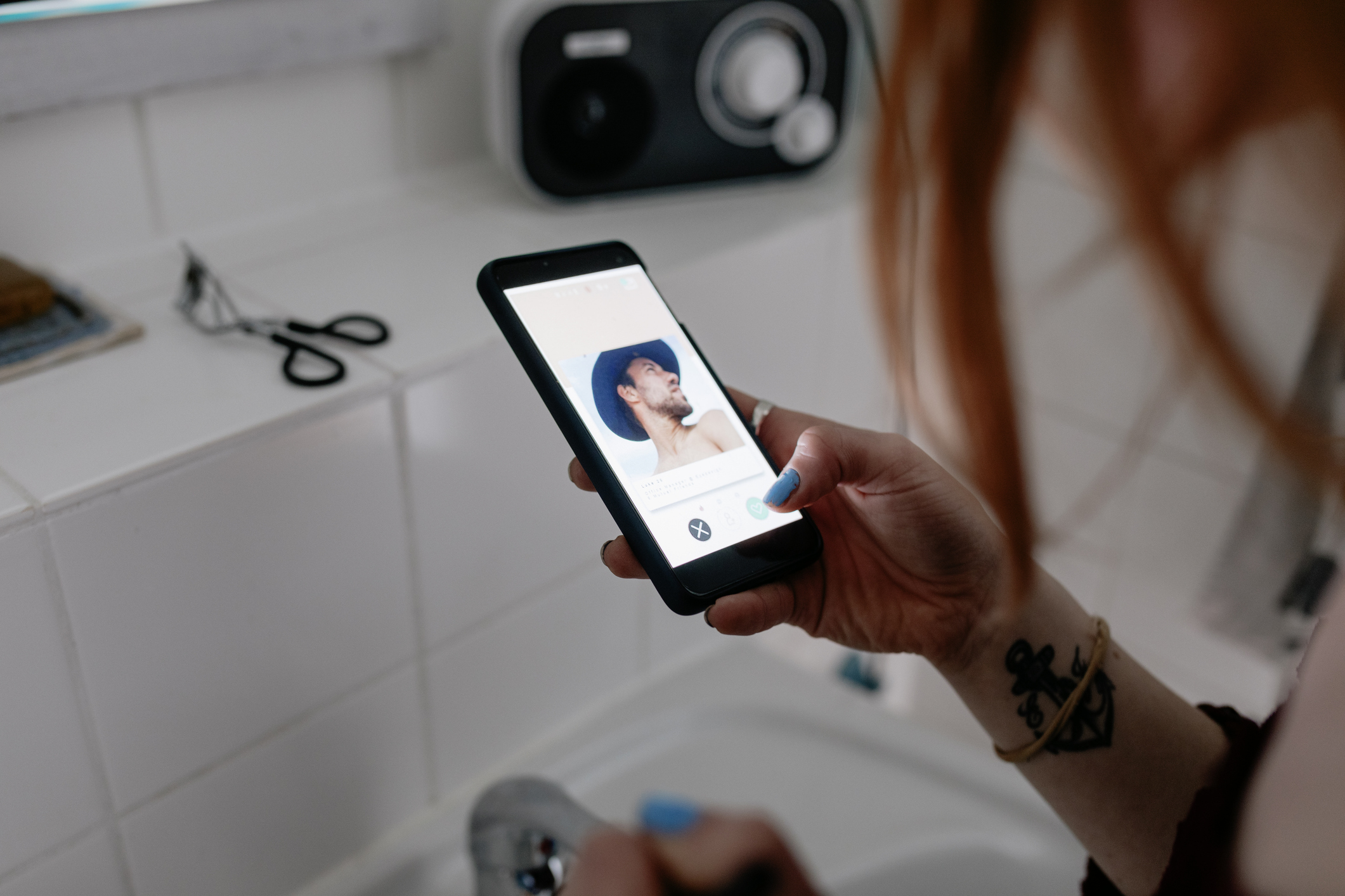 Person holding a phone displaying a dating profile picture of another person by a sink with personal grooming tools
