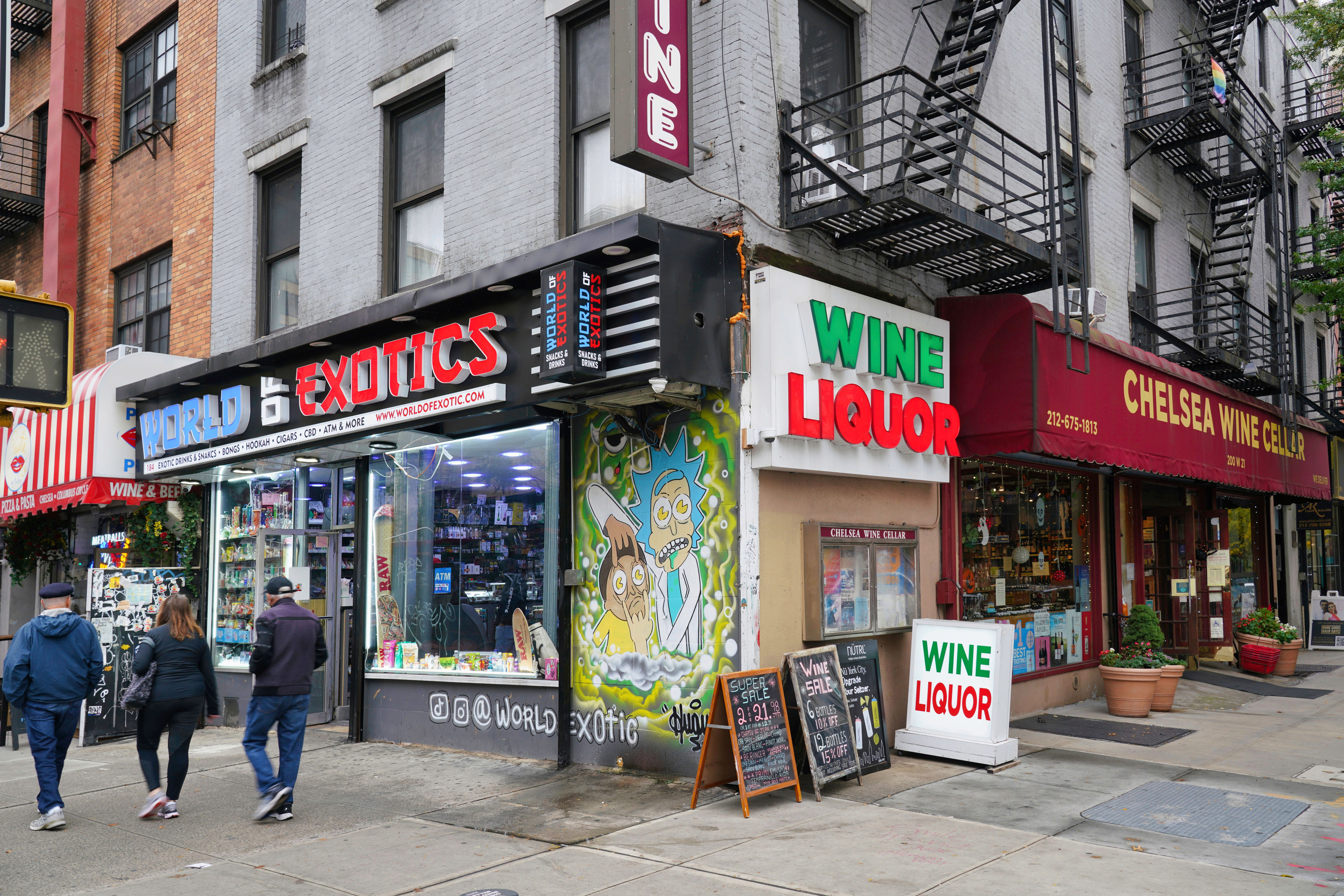 Exterior of &quot;World Exotics&quot; next to &quot;Chelsea Wine Cellar&quot; and &quot;Wine Liquor&quot; shops on a city street. Three people are walking past the stores
