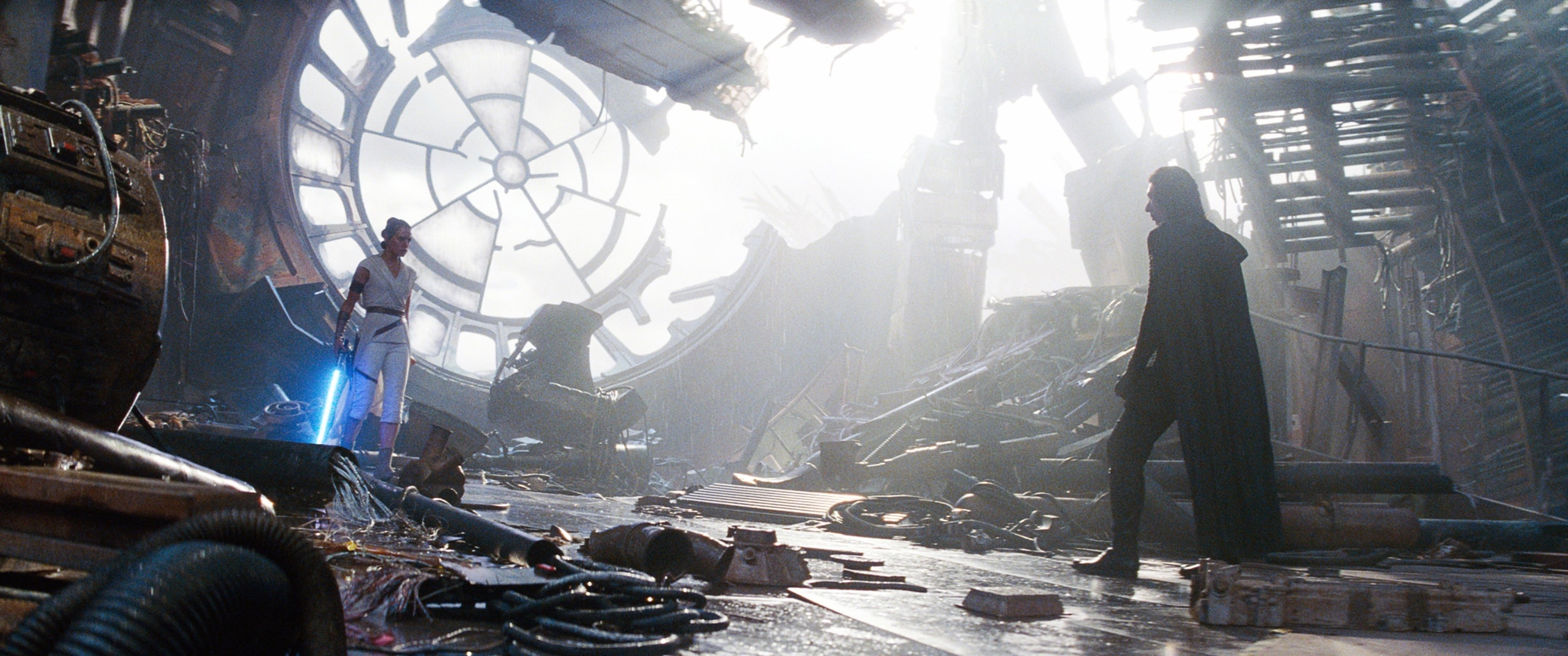 Rey faces Kylo Ren in a dramatic battle scene from "Star Wars: The Rise of Skywalker." Rey wields a lightsaber. The setting is a wrecked, futuristic structure