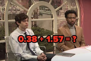 Pete Davidson in a striped shirt and tie and Donald Glover in a tan blazer and turtleneck sit at a desk in a studio with a cityscape background