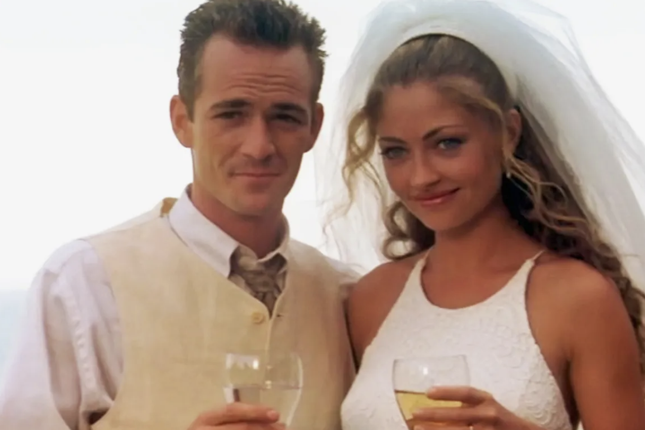 Luke Perry in a beige vest and Christine Elise in a white wedding dress with a veil, holding drinks