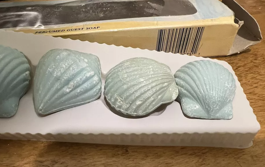 Three shell-shaped, perfumed guest soaps on a white tray with their packaging visible in the background