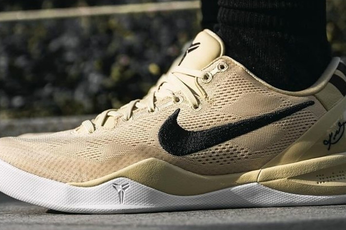 Close-up of a person wearing beige Nike sneakers with a signature black swoosh and a Kobe Bryant logo on the toe and sole