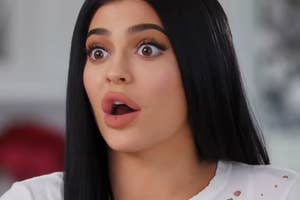 Kylie Jenner with long, straight hair, wide-eyed expression, wearing a white top