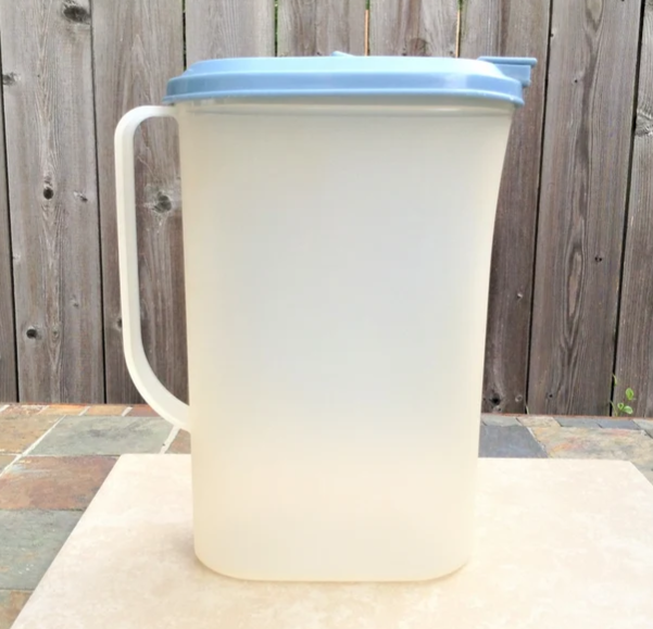 A clear plastic pitcher with a lid, placed on a table in front of a wooden fence