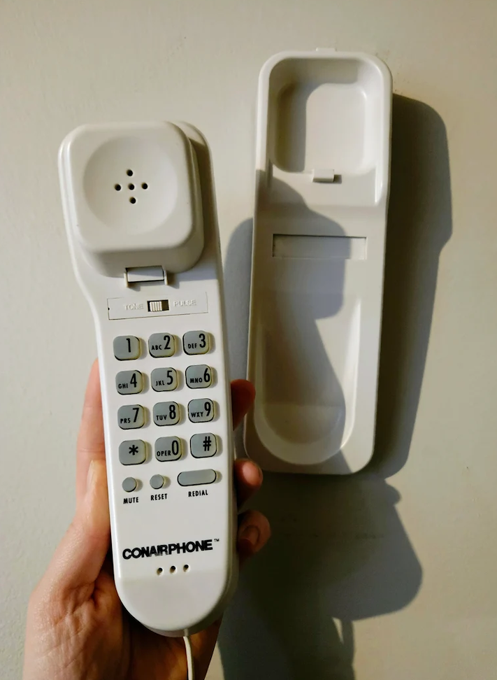 A hand holds a ConairPhone corded telephone with its receiver detached from the base, showing the number pad and buttons