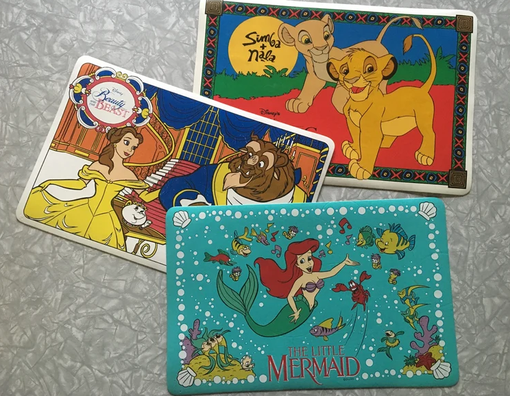Beauty and the Beast, The Lion King, and The Little Mermaid-themed placemats featuring Belle, the Beast, Simba, Nala, and Ariel in various scenes from their movies
