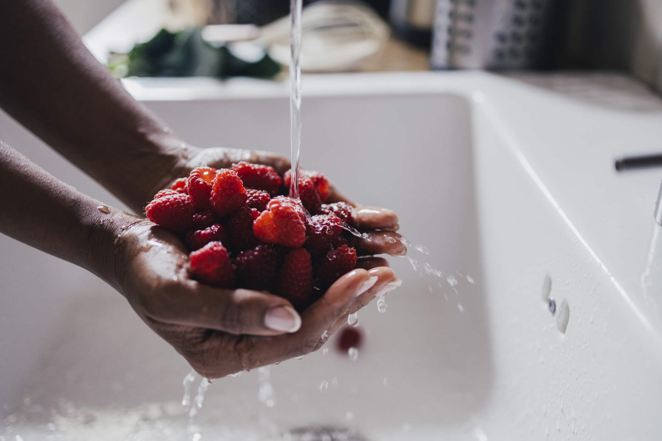 Person washing handful of raspberries under running water in a sink