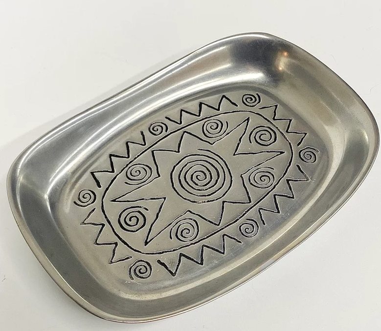 A rectangular metal tray with a decorative design featuring spirals and zigzag patterns around a large central spiral