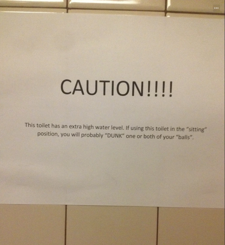 Sign warning that toilet has an extra high water level. It humorously cautions male users that sitting may cause them to "dunk" their genitalia