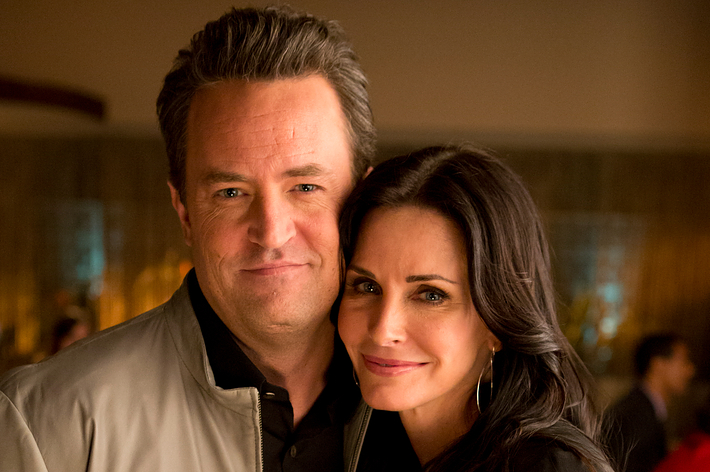 Matthew Perry and Courteney Cox smiling and posing together. Matthew is wearing a casual jacket, and Courteney is in a simple elegant top