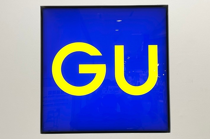 Artwork featuring “GU” in bold letters against a blue background, displayed in a gallery setting