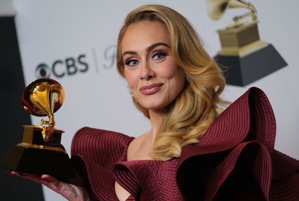 Adele holds a Grammy award while wearing an elegant gown with ruffled sleeves at a CBS event