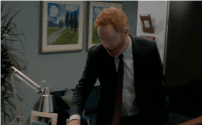 Jesse Tyler Ferguson as Mitchell Pritchett franticly looking for something on his desk in an office, from the TV show Modern Family, streaming on Hulu