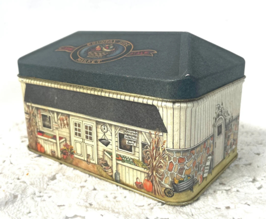 Rectangular decorative tin box with a nostalgic market scene on its sides showcasing a storefront, pumpkins, and corn stalks. No text or people are depicted