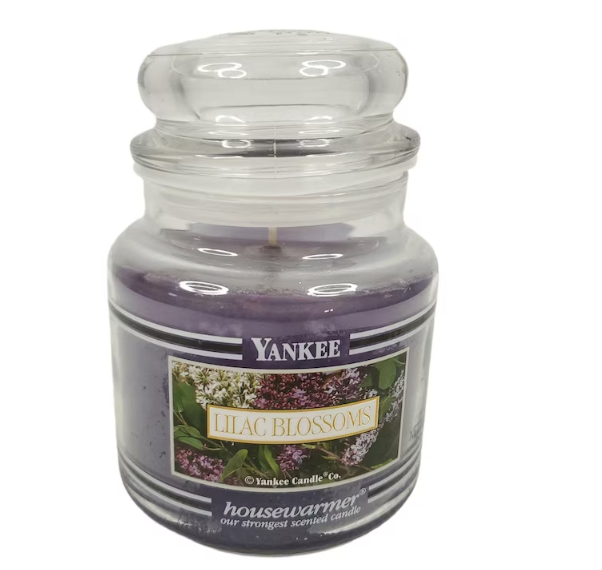 Yankee Candle &quot;Lilac Blossoms&quot; scented candle in a glass jar. Lid is on top. The label shows lilac flowers and reads &quot;Lilac Blossoms, housewarmer.&quot;