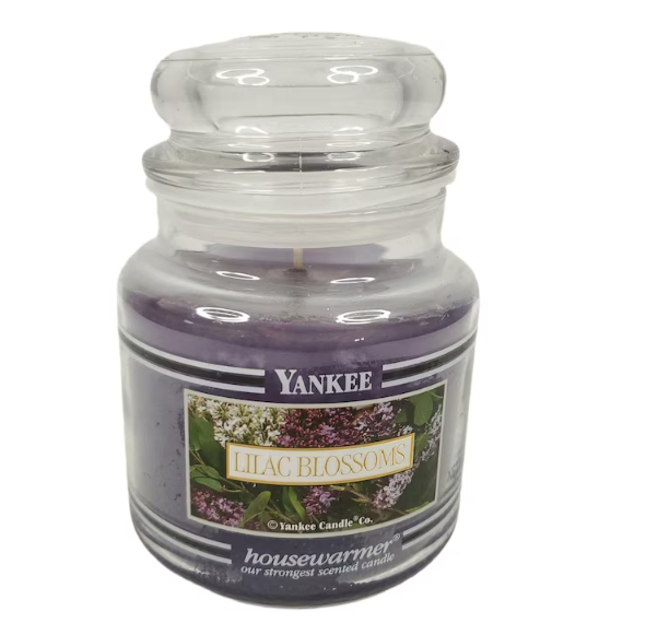 Yankee Candle "Lilac Blossoms" scented candle in a glass jar. Lid is on top. The label shows lilac flowers and reads "Lilac Blossoms, housewarmer."
