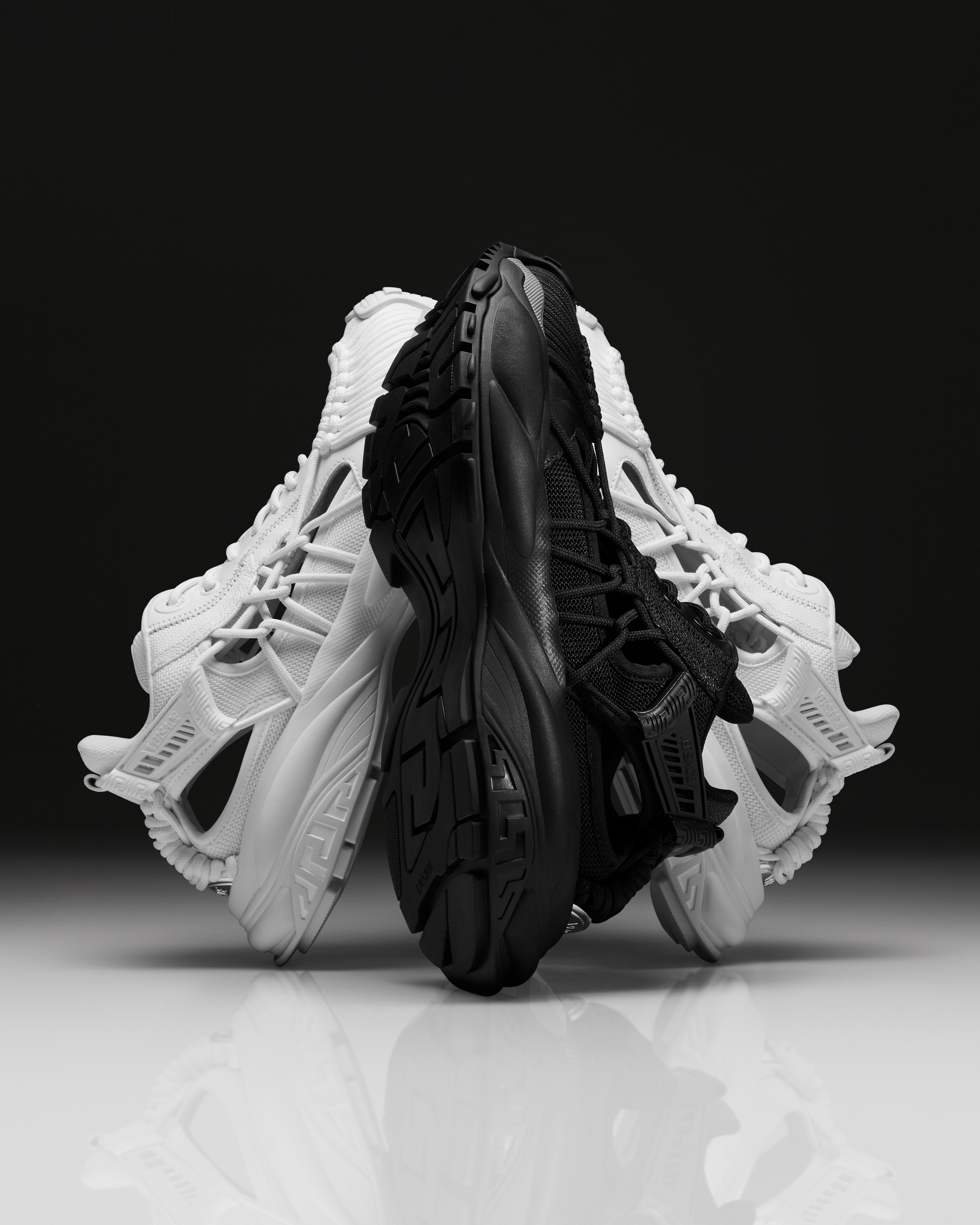A pair of white sneakers and a pair of black sneakers are arranged artfully with their soles facing out, creating a dynamic, symmetrical display