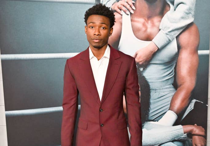 Niles Fitch wearing a dark suit with a shirt stands on the red carpet