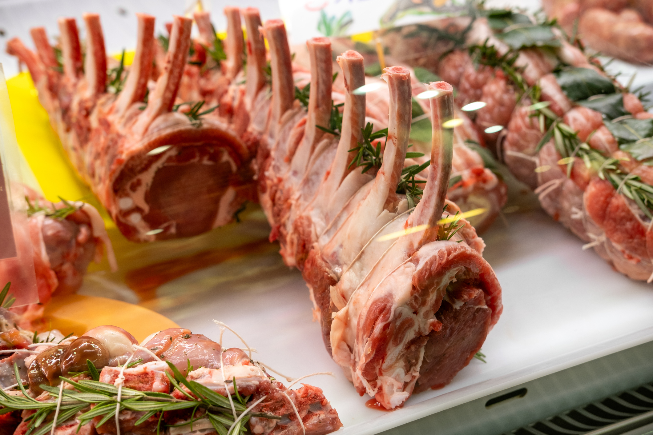 Various uncooked lamb racks garnished with rosemary on display at a butcher's counter