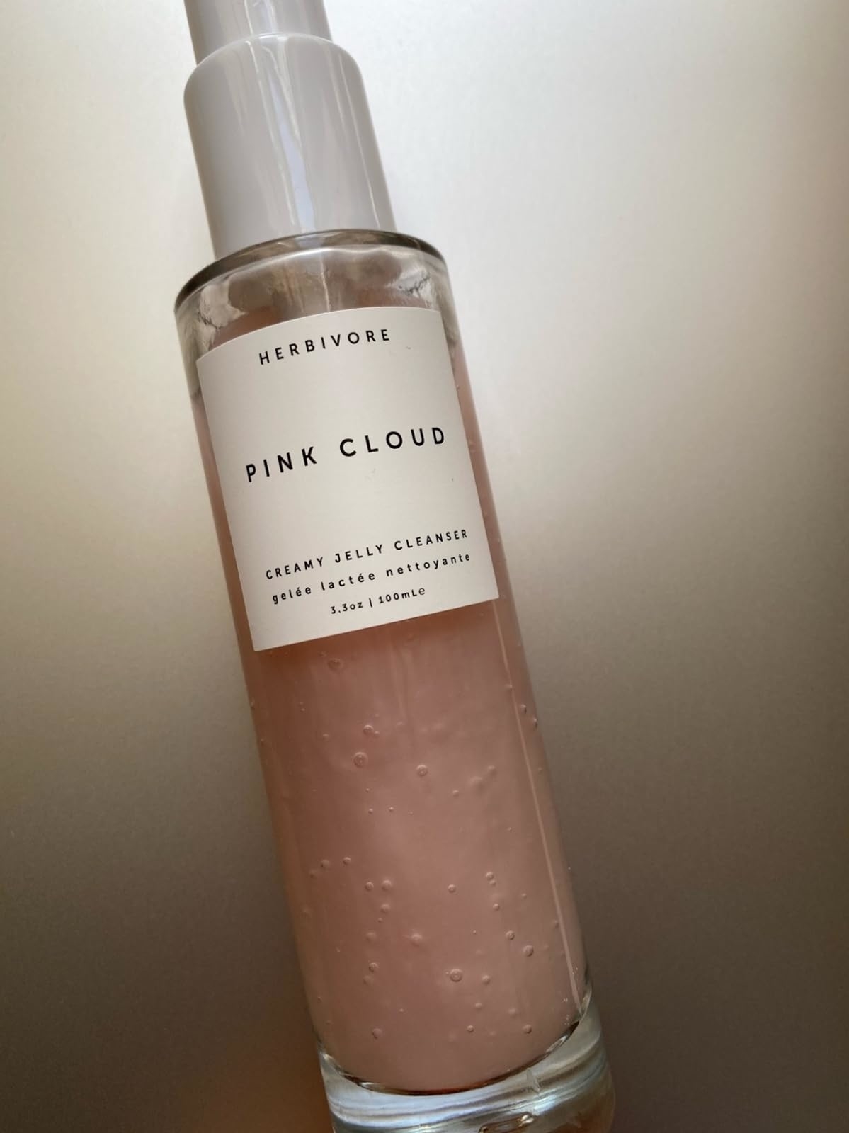 A reviewer's photo of Herbivore Pink Cloud Creamy Jelly Cleanser bottle with visible light pink gel inside