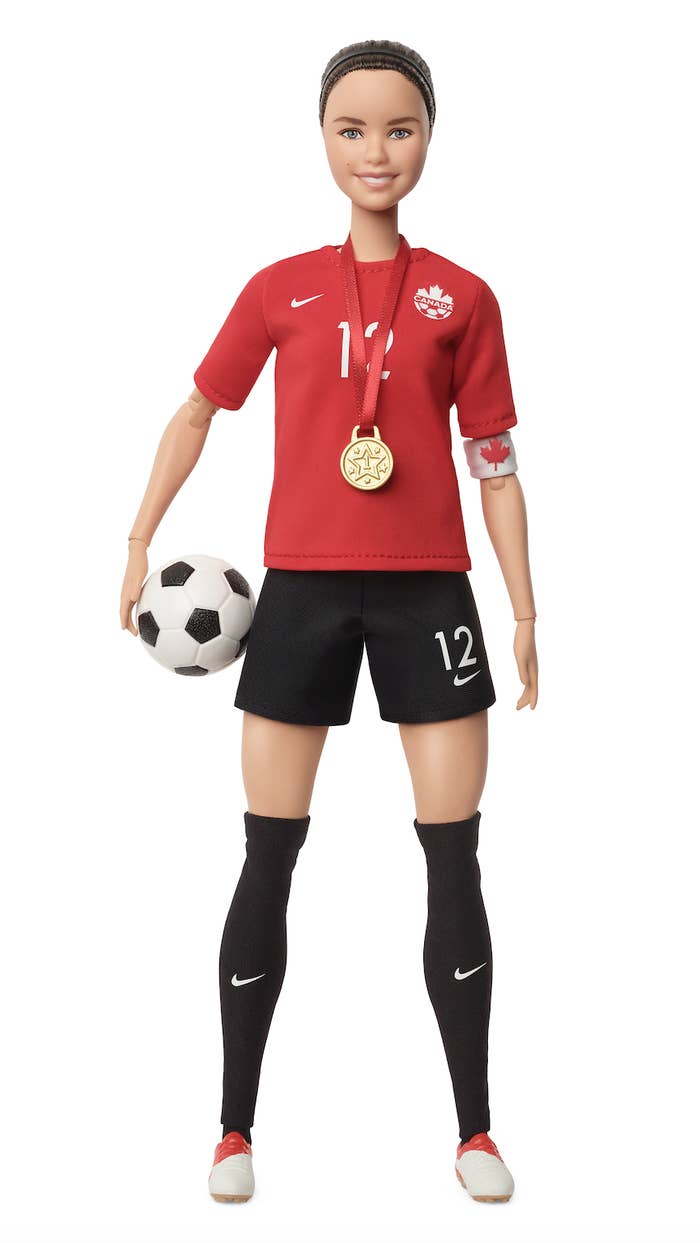 Barbie doll in a soccer uniform with a Canadian logo, holding a soccer ball and wearing a medal, representing soccer player Christine Sinclair