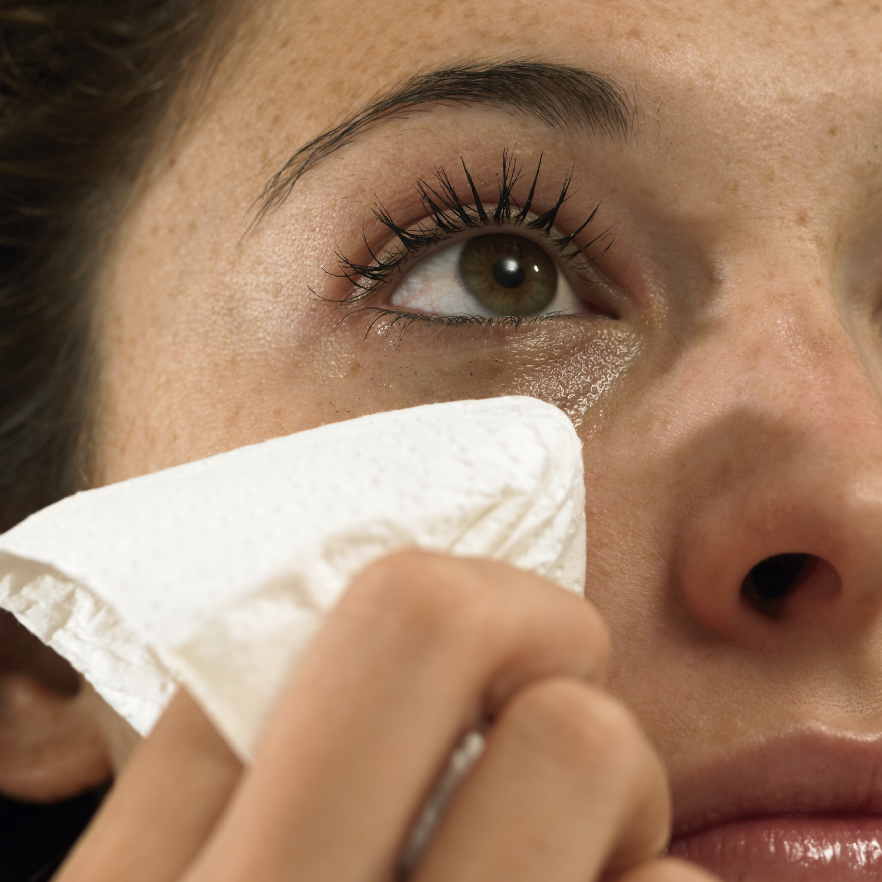 Close-up of a person's face as they wipe a tear with a tissue