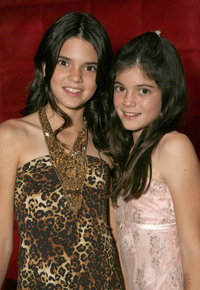 Kendall Jenner in a leopard print strapless dress and Kylie Jenner in a light pink dress with floral embroidery, posing together and smiling
