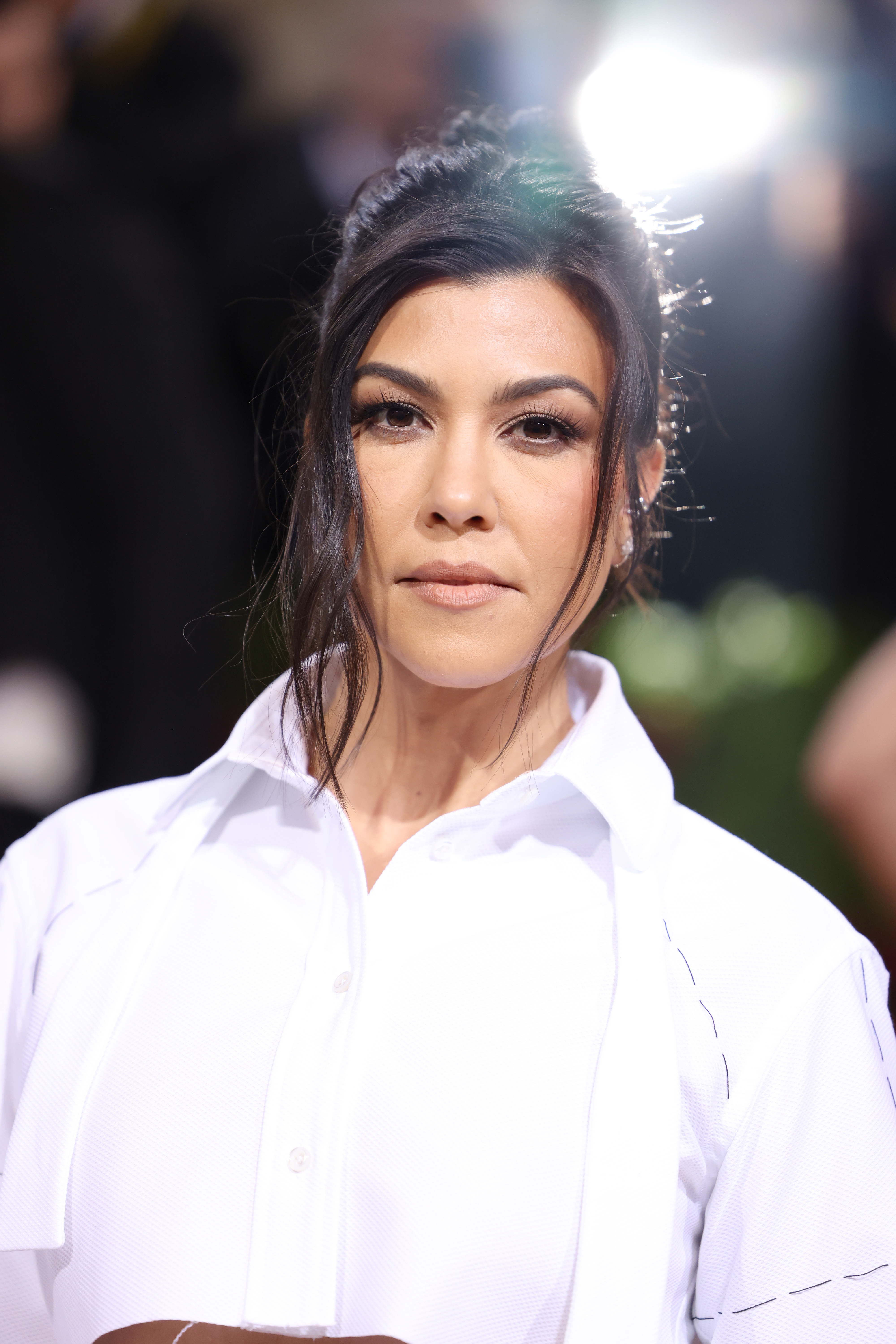 Kourtney Kardashian at a formal event, wearing an elegant dress shirt with her hair styled in an updo
