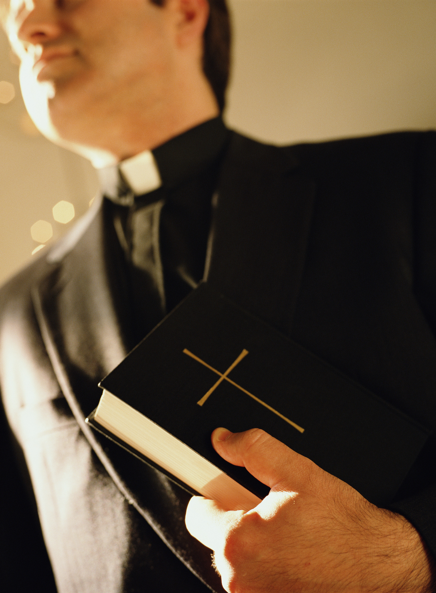 A person dressed in a priest's attire holds a book with a cross on the cover