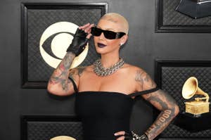 Amber Rose on a red carpet wearing a black strapless dress, black sunglasses, black gloves, and silver necklace and bracelets, with tattoos visible on her arms