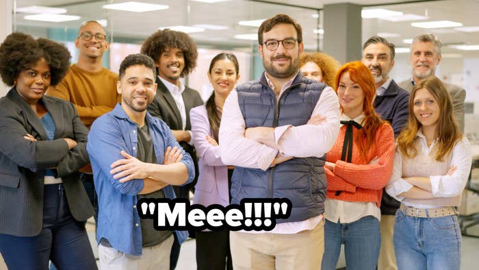 Group photo of 12 people, including three men and three women in business casual attire, standing in an office setting with glass walls