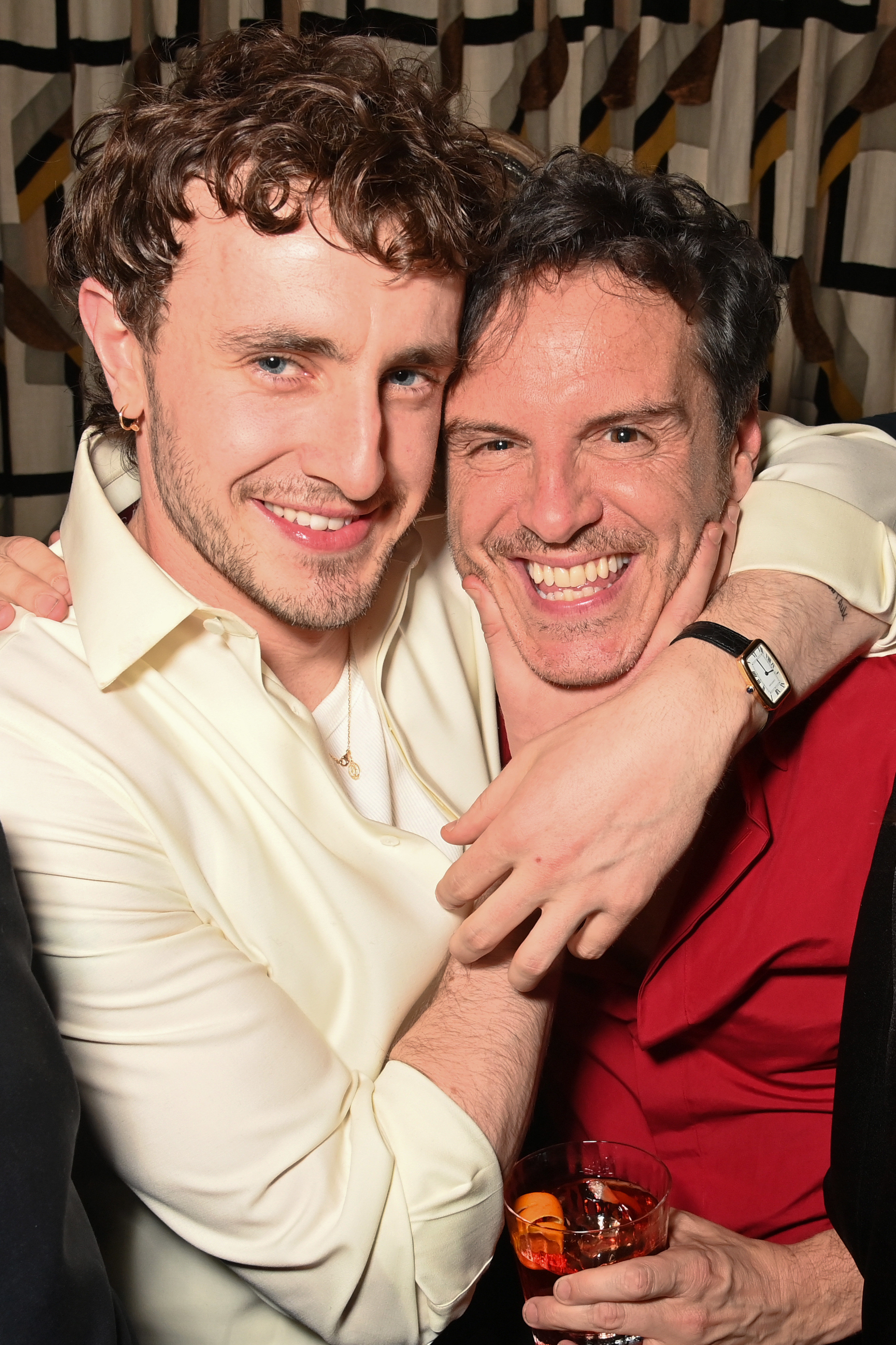 Paul Mescal and Andrew Scott smiling and embracing at an event, Andrew holding a drink