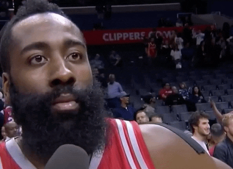 James Harden in a post-game interview, wearing a basketball jersey with fans and stadium seats in the background