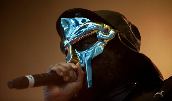 MF DOOM performing on stage, wearing his iconic metal mask and holding a microphone