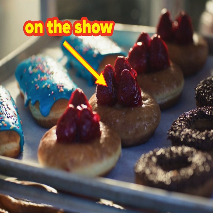 A close-up of a tray of assorted donuts, including donuts with blue icing and sprinkles, donuts with strawberries on top, and chocolate-coated donuts