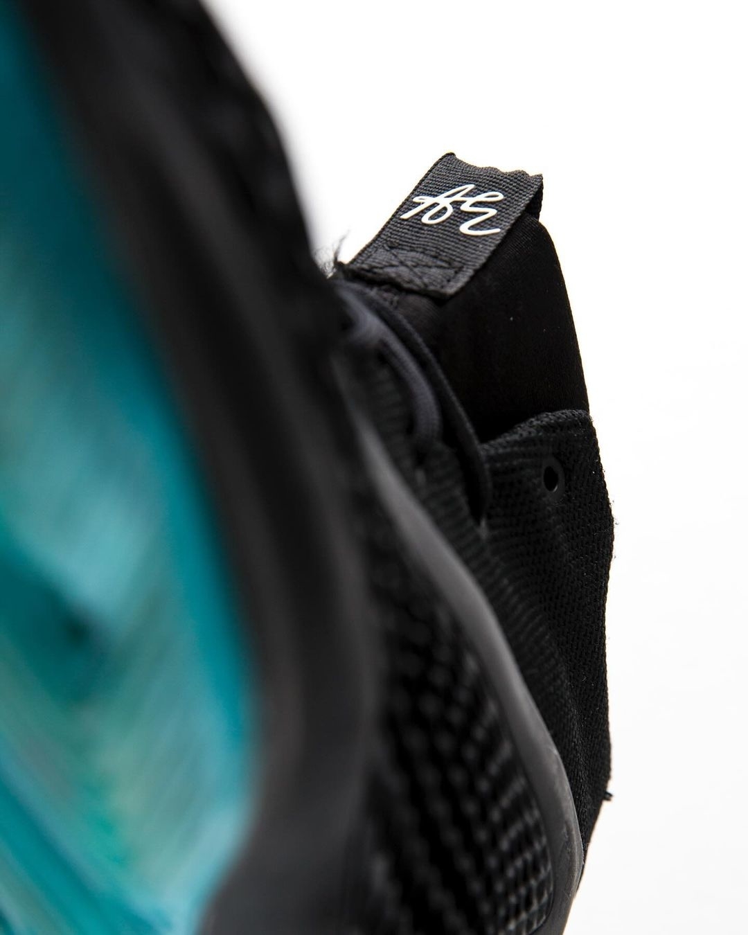 Close-up view of a black sneaker, focusing on the heel area with visible blue sole detail and a tag with a white logo