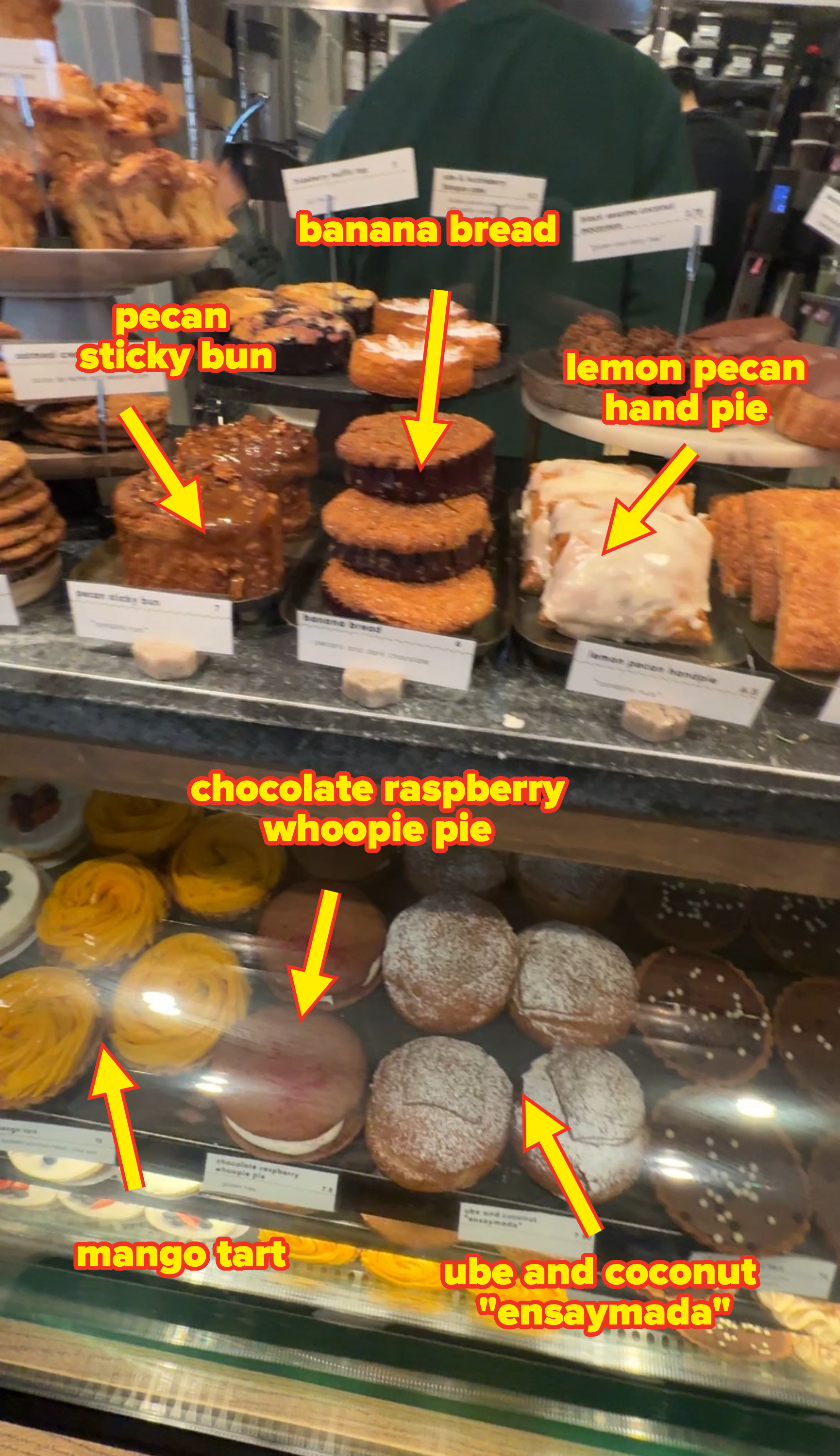 A bakery display case featuring various pastries, including cookies, cakes, and donuts, with labels indicating their names and prices