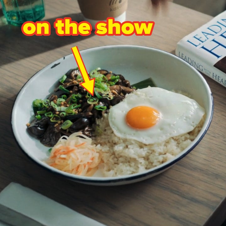 A bowl of rice with a sunny-side-up egg, veggies, and sautéed meat on a table next to a cup and an open book titled "Leading with the Heart" by Mike Krzyzewski
