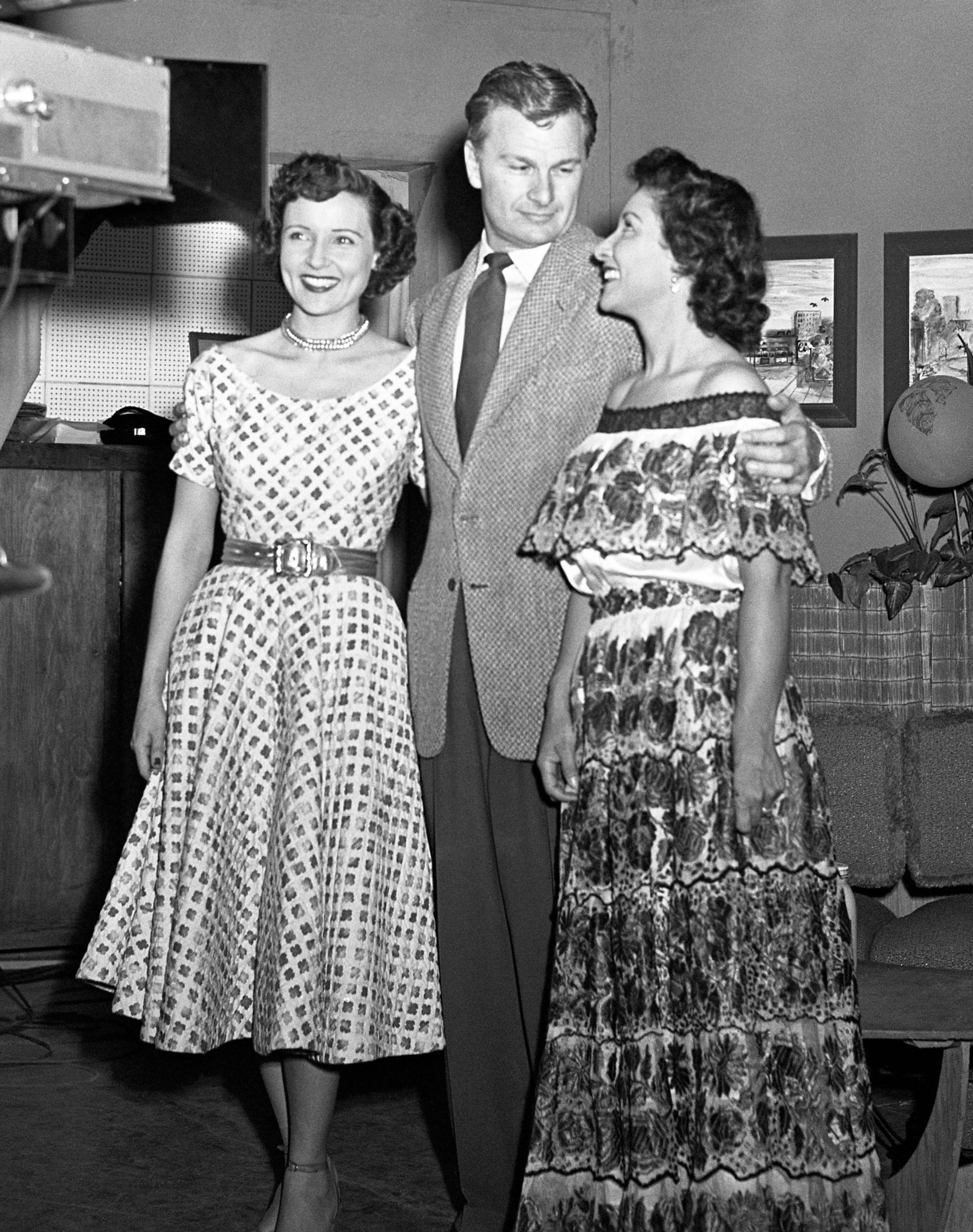Three people stand together in a TV studio set, with a camera operator in the foreground