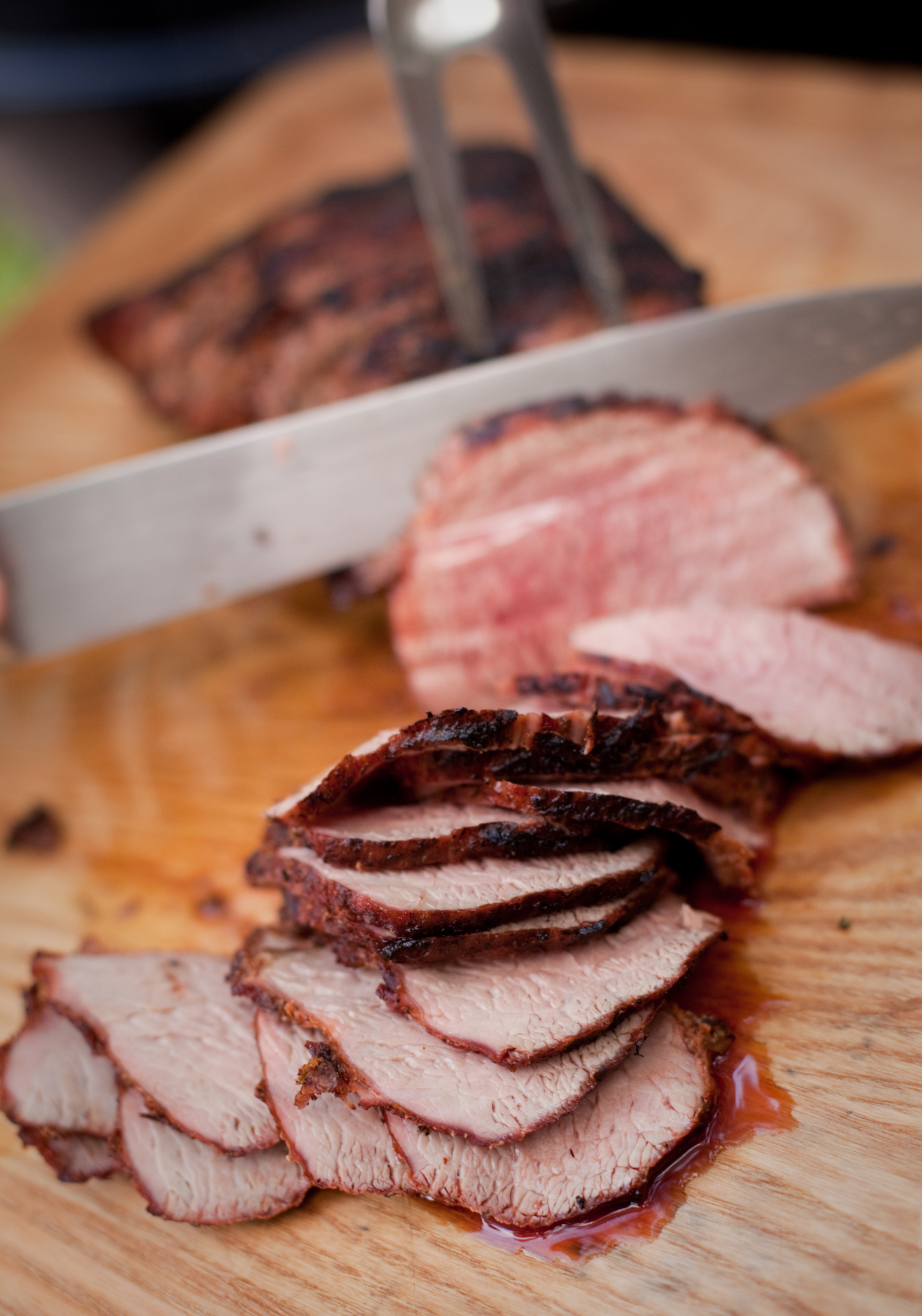 A person is slicing a well-cooked steak into thin slices on a wooden cutting board
