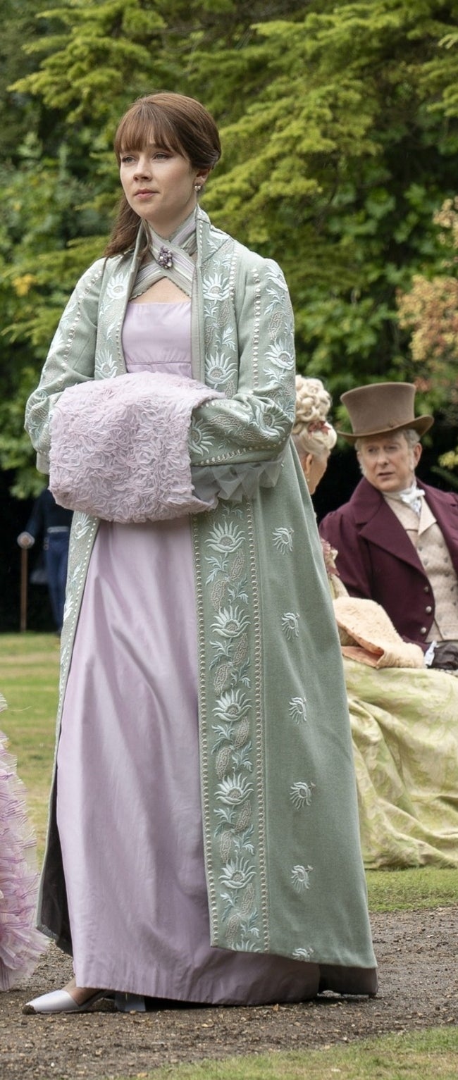 Eloise walking in a Regency dress with her arms in a muff