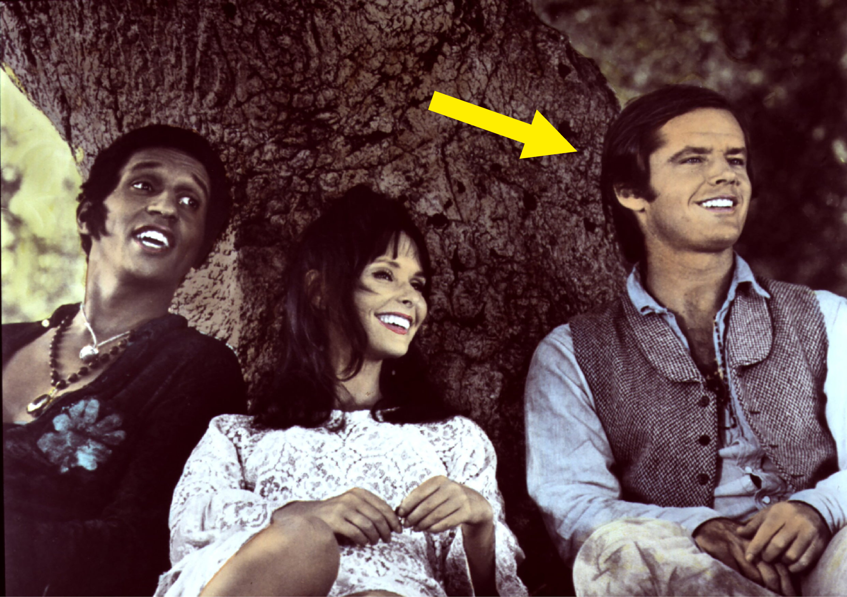 From left to right, Toni Basil, Karen Black, and Jack Nicholson are sitting together, smiling, and relaxing against a tree