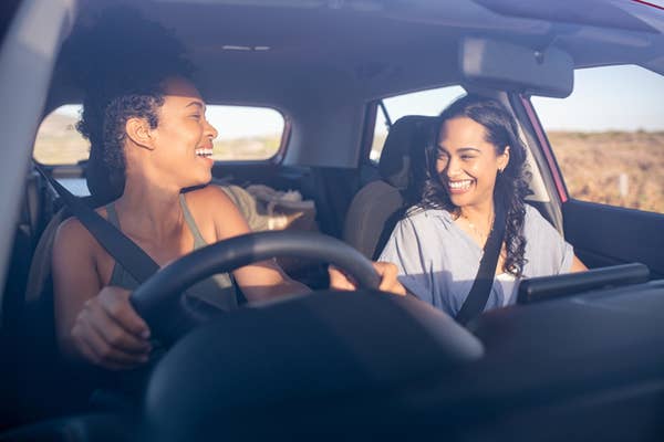 Two women smile and share a joyful moment while driving a car on a sunny day
